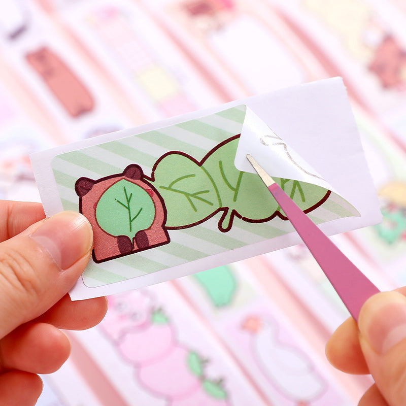 Hand holding a small card with a cartoon capybara design against a blurred background