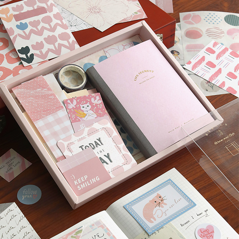 journal set with pink notebook, stickers, and other items in a box on a wooden surface.
